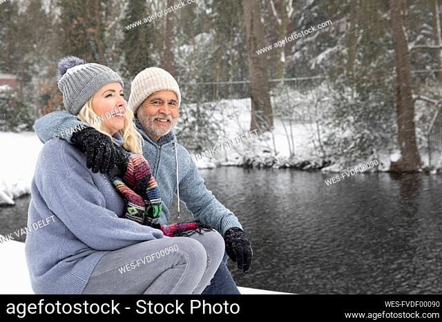 Man embracing woman while sitting near lake during winter