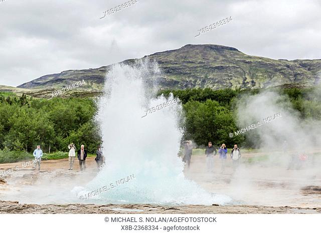 Strokkur geyser erupting while tourists watch in the Haukadalur valley on the slopes of Laugarfjall hill, near the Hvítá River, Iceland