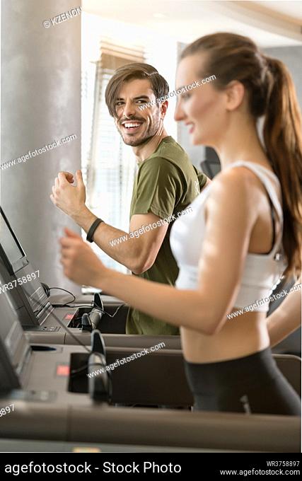 Determined young man smiling while running on treadmill during high-intensity interval training