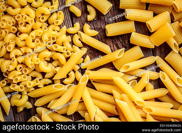 Close up mix of raw dried talian pasta, macaroni, spaghetti, penne om wooden table. Top view