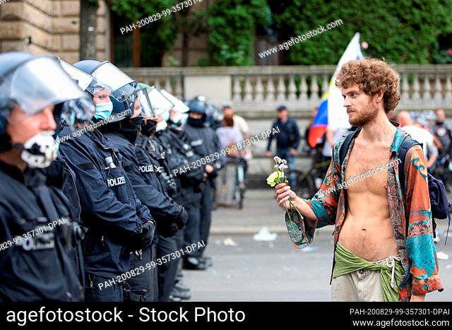 dpatop - 29 August 2020, Berlin: A demonstrator holds flowers in front of police officers in a protest against the Corona measures in front of the Russian...