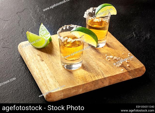 Golden tequila shots with lime slices and salt rims on a black background
