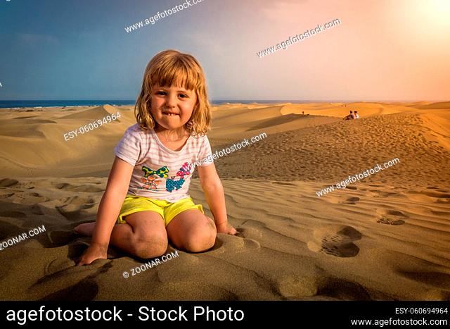 Little girl sitting on the sand on the sand dunes in the Natural Reserve of Dunes of Maspaloma in Gran Canaria