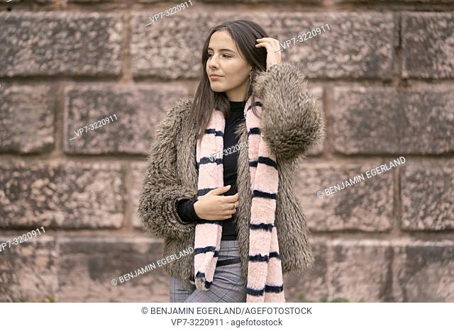 woman in front of stone wall, wearing winter clothes, in city Munich, Germany