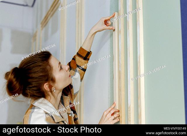 Young woman sticking wood on wall in apartment