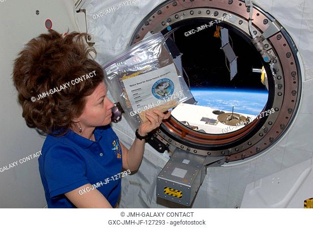 NASA astronaut Cady Coleman, Expedition 27 flight engineer, holds a bag of space seeds near a window in the Kibo laboratory of the International Space Station