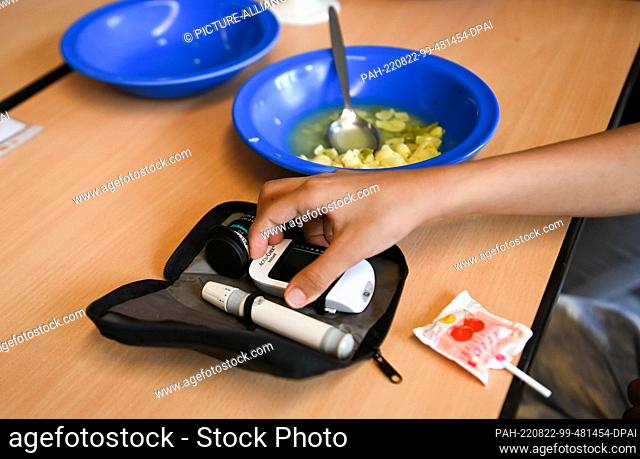 22 August 2022, Berlin: A girl reaches for her blood glucose meter next to her lunch at the school in Köllnische Heide in Neukölln on the school desk in the...