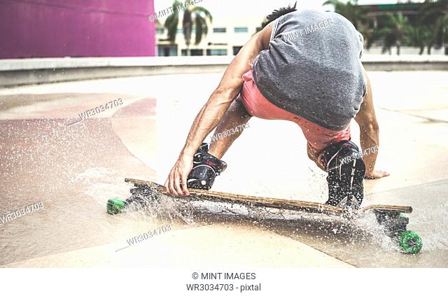 A skateboarder crouching down riding a skateboard through water