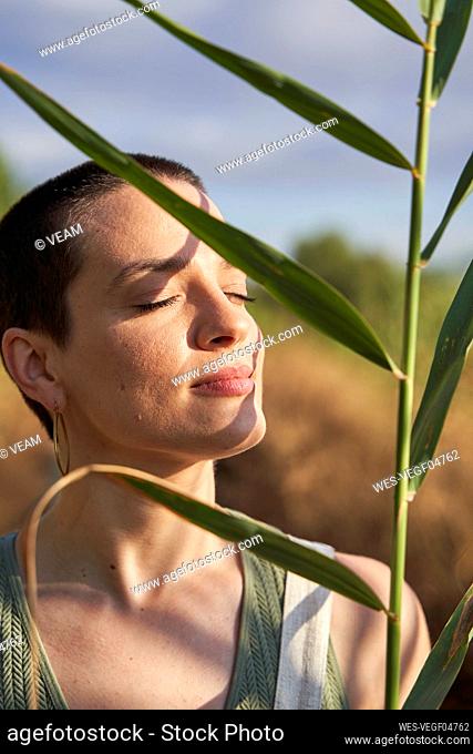 Young woman eyes closed holding leaves on sunny day