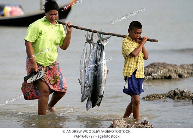 Woman and boy carry Spanish Mackerel on pole Ban Batu fishing village Ko Libong island Thailand