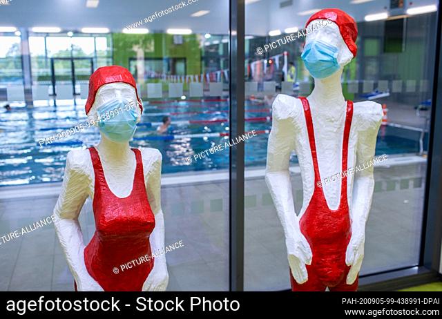 03 September 2020, Mecklenburg-Western Pomerania, Wismar: Two figures with swimwear and mouth-and-nose protection stand in the entrance area of the indoor pool