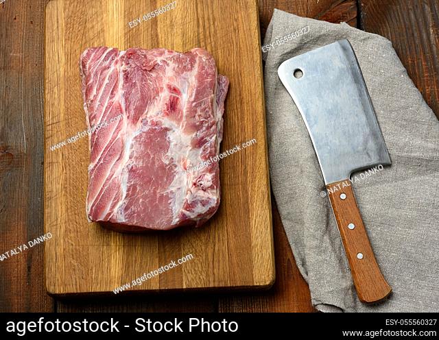 knife and raw pork tenderloin on a wooden cutting board, top view