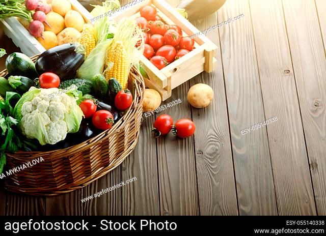Basket of Organic Vegetable Food Ingredients and crates of potatoes and tomatoes on wood background