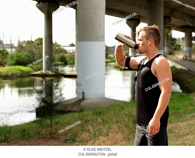 Young man beside river, drinking from water bottle