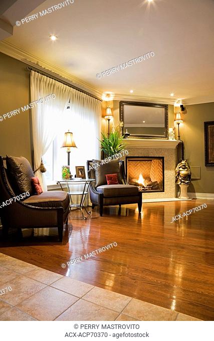 Family room with a gas fireplace and hardwood floor inside a luxurious cottage style residential home, Montreal, Quebec, Canada