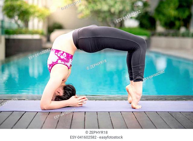Beautiful young Asian woman doing yoga exercise near swimming pool. Healthy lifestyle and good wellness concepts