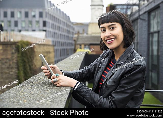 Woman on mobile phone standing at ledge of building on rooftop patio