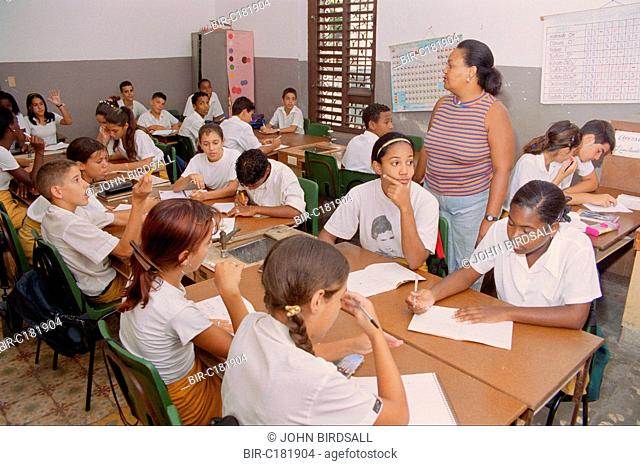 Secondary school children sitting at desks in classroom with teacher