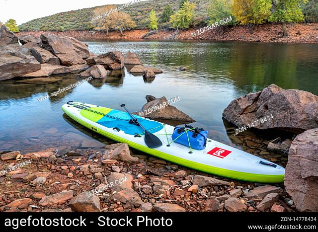 Fort Collins, CO, USA - October 15, 2019: inflatable stand up paddleboard by Red Paddle Co with waterproof bag and paddle on a rocky shore of mountain lake -...