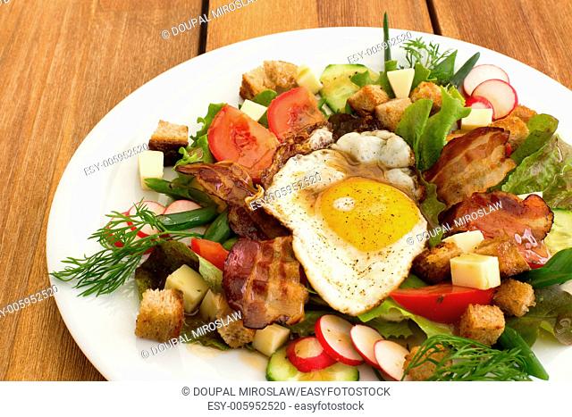 Peasant salad also called greek salad, village salad or country salad. Composed with lettuce, cucumber, onion, radish, fried egg and bacon, cheese, tomatoes