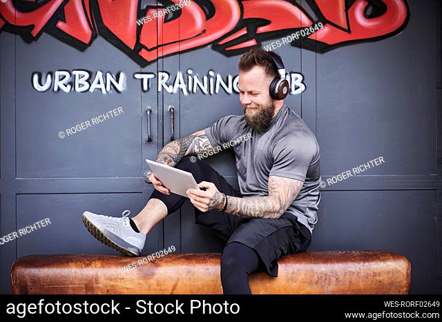 Smiling male athlete using digital tablet outside gym against graffiti door