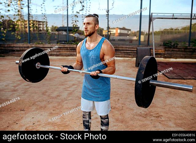 Strong man doing exercise with barbell, street workout. Fitness training on sports ground outdoor, male person pumps muscles, active urban lifestyle