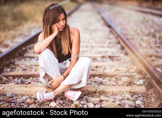 Sad young woman sitting on the railway
