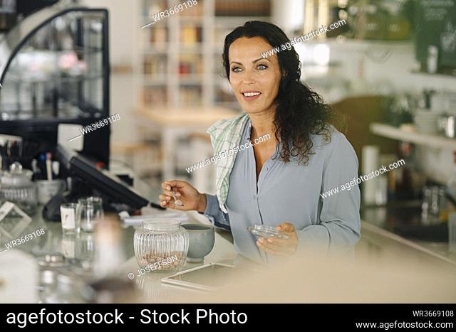 Smiling female barista looking away while working at counter in cafe