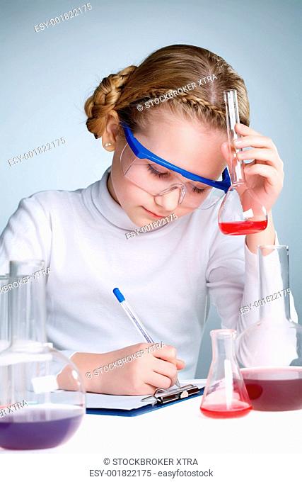 A little girl holding a flask with liquid and making notes