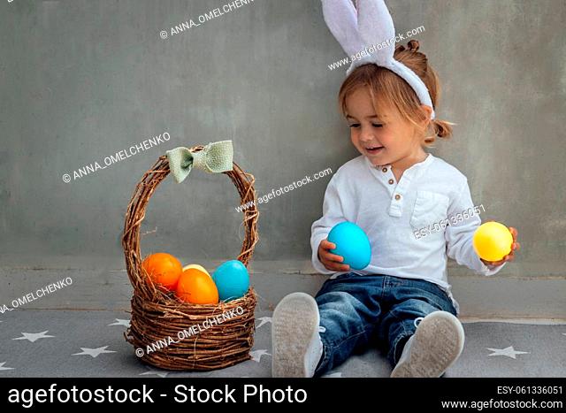 Portrait of Cute Little Baby Boy with Nice Rabbit Ears. Basket Full of Colorful Eggs. Happy Easter Celebration