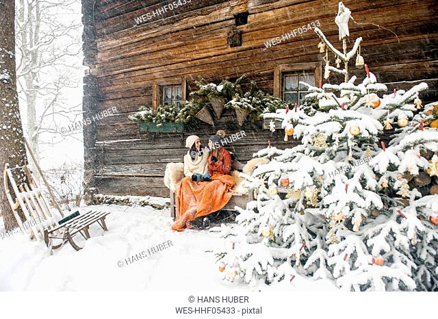 Friends sitting on bench by Christmas tree in front of mountain hut