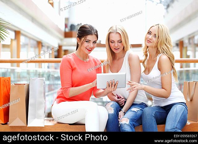Young beautiful happy female friends with tablet pc and shopping bags in mall