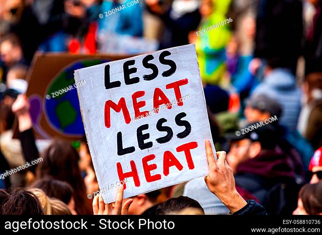 A close-up shot of a homemade poster, saying less meat less heat, being held above a crowded street of environmental demonstrators