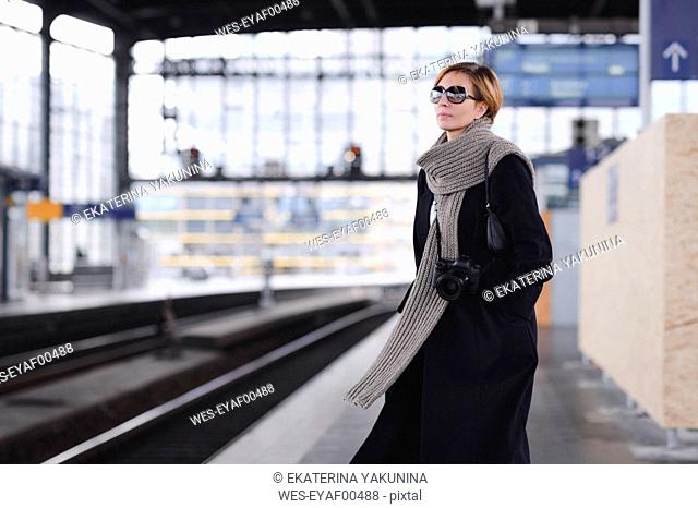 Mature woman with camera wearing black coat and large wool scarf waiting at platform