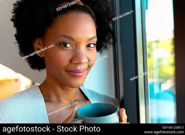 Portrait of confident smiling young african american afro woman holding coffee cup at home