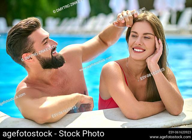 Man in love sitting in the swimming pool and stroking the hair of his beautiful girlfriend