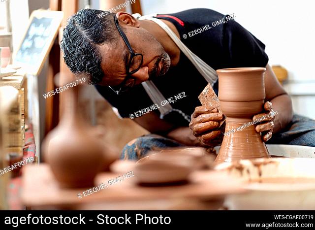 Close-up of male artist making earthenware on pottery wheel in workshop