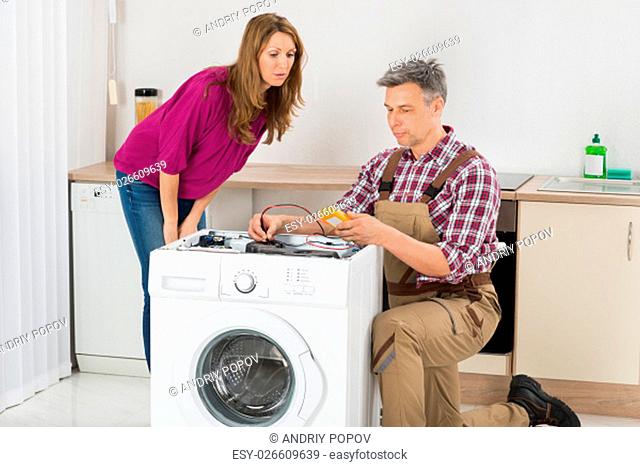Woman Looking At Male Technician Checking Washing Machine In Kitchen