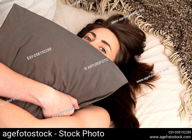 Beautiful woman holding a pillow in front of her face while looking at camera. Lazy sunday