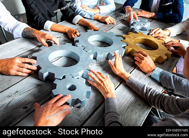 Group of business people joining together silver and golden colored gears on table at workplace
