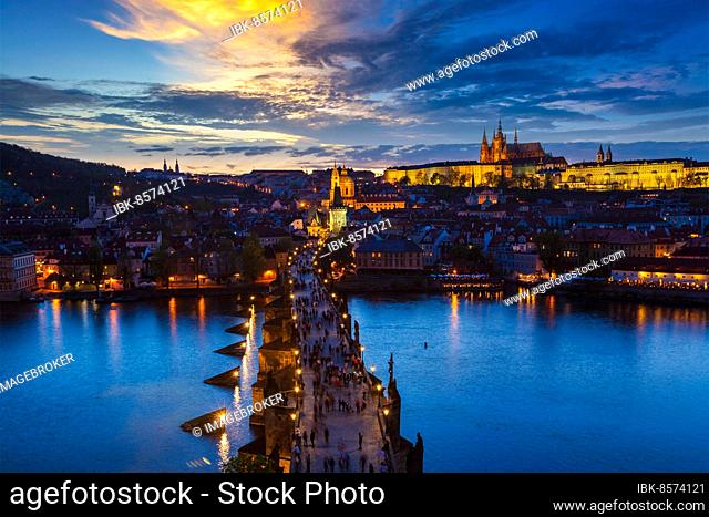 Aerial view of illuminated Prague castle and Charles Bridge with tourist crowd over Vltava river in Prague, Czech Republic