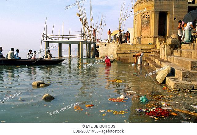 Scum and remnants of flower offerings float around the steps of the ghats on the River Ganges