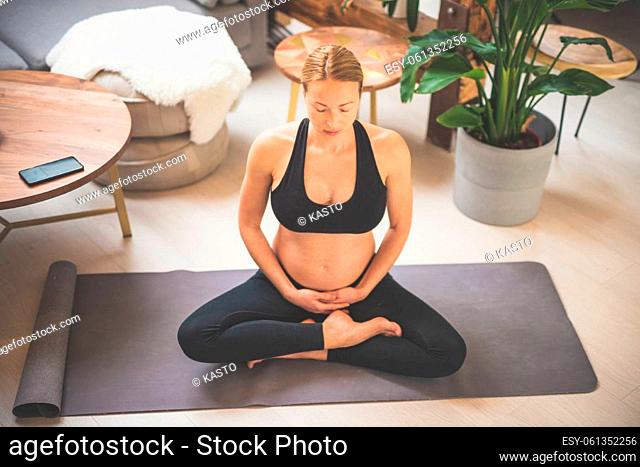 Young beautiful pregnant woman training yoga, caressing her belly. Young happy expectant relaxing, thinking about her baby and enjoying her future life