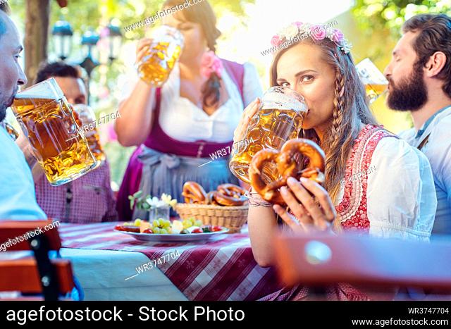 Woman in Tracht looking into camera while drinking a mass of beer surrounded by her friends