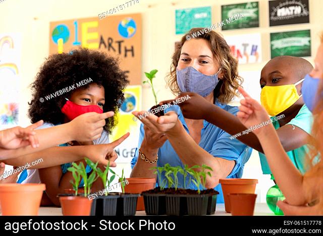 Female teacher wearing face mask showing plant pots to students in class