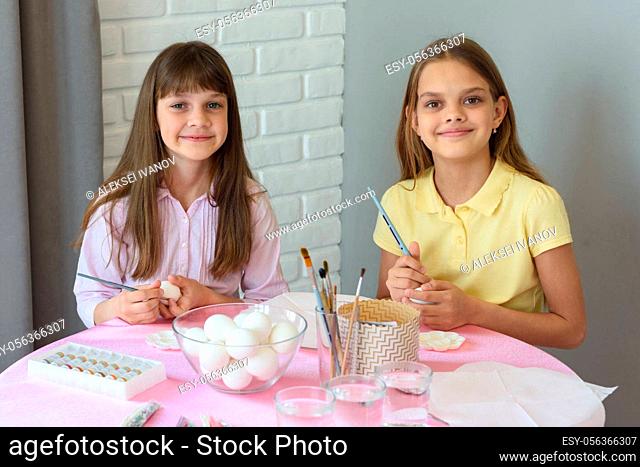 Children are preparing to paint Easter eggs while sitting at a table in a home environment