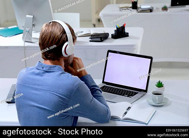 Caucasian businessman having video call meeting using laptop and headphones in empty office