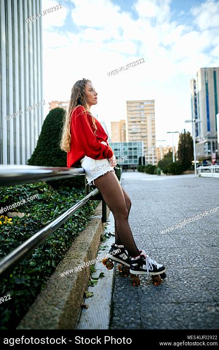 Young woman on roller skates leaning against railing in the city