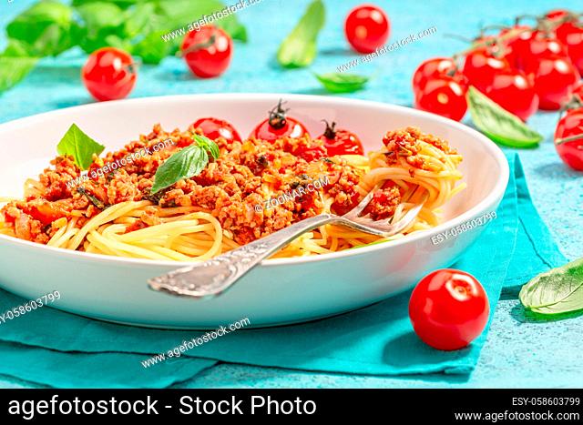 Fork in a plate with macaroni, meat tomato sauce, fresh basil and caramelized tomatoes, selective focus