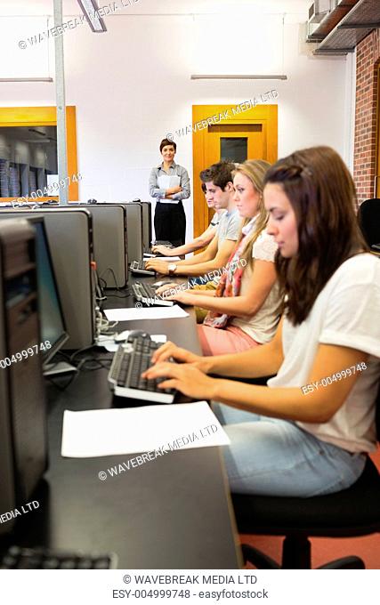 Student sitting at the computer concentrating while teacher standing in college